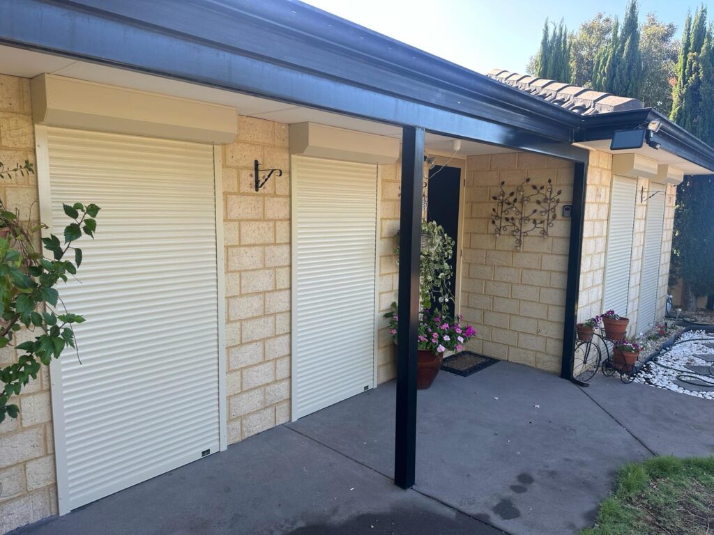 Cream-colored roller shutters fitted to light brick windows under a covered home patio area.