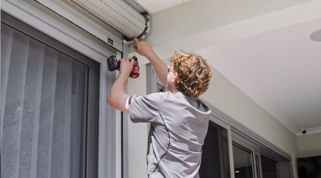 Professional installation of a motorised roller shutter on a commercial building by an MCF Master Group technician