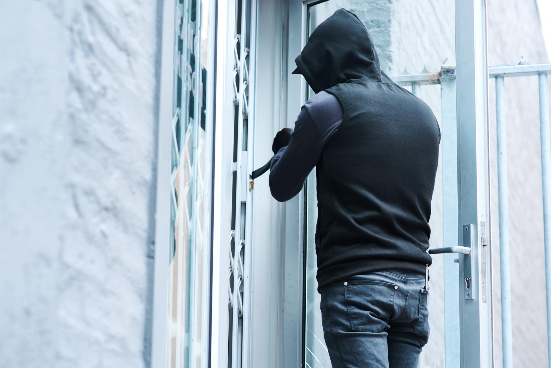 A hooded burglar attempting to pry open a glass commercial door.