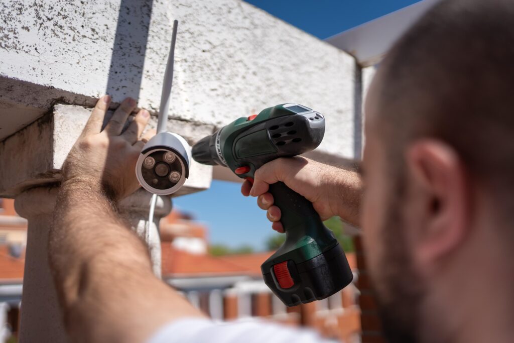 A technician using a power drill to install an exterior security camera.