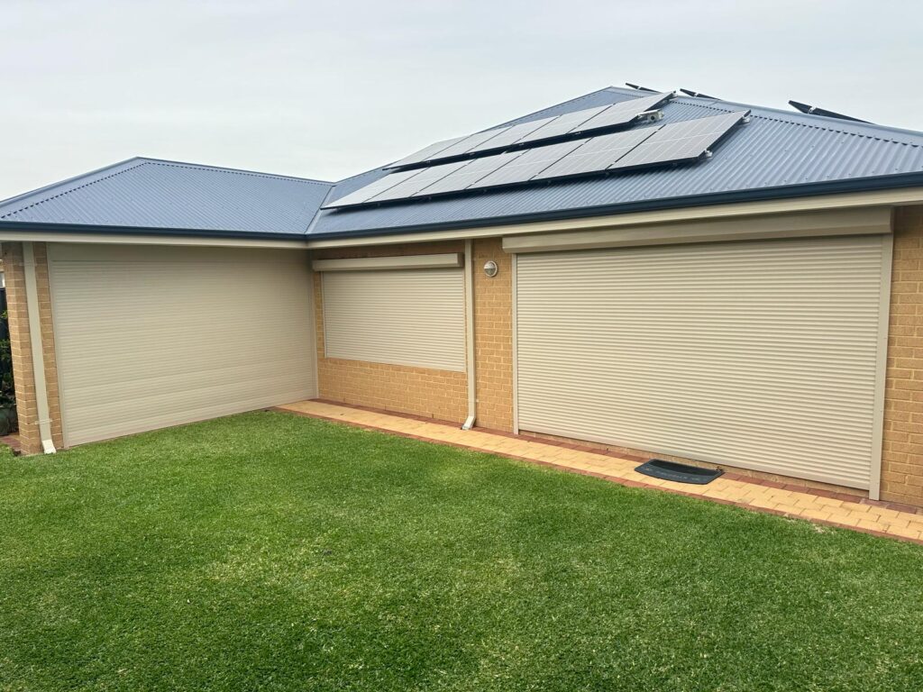 Beige roller shutters on a brick house with solar panels, providing thermal insulation, privacy, and security alongside noise control