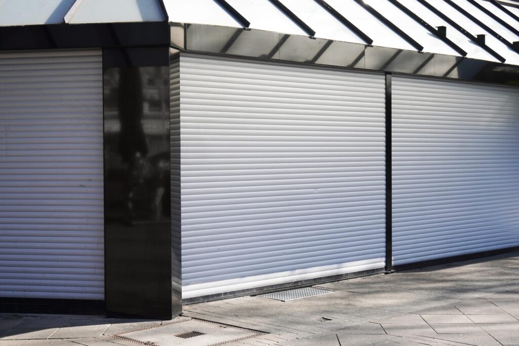 A commercial storefront secured with closed aluminium roller shutters, offering physical protection.