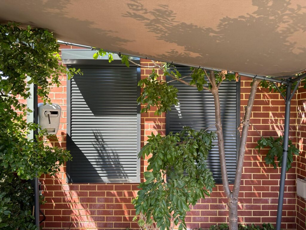 A dark grey roller shutter fully closed on a red brick home, illustrating a properly sealed installation needed for real noise reduction