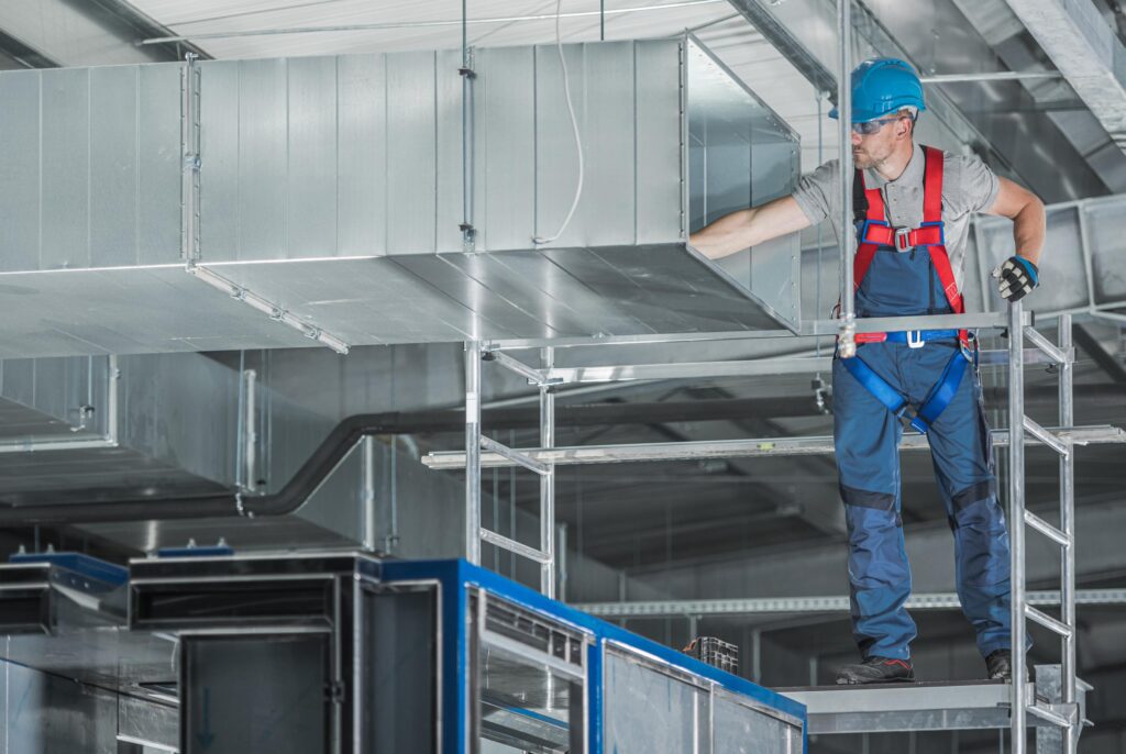 Worker on scaffolding inspecting commercial HVAC ductwork, highlighting the need for building automation.